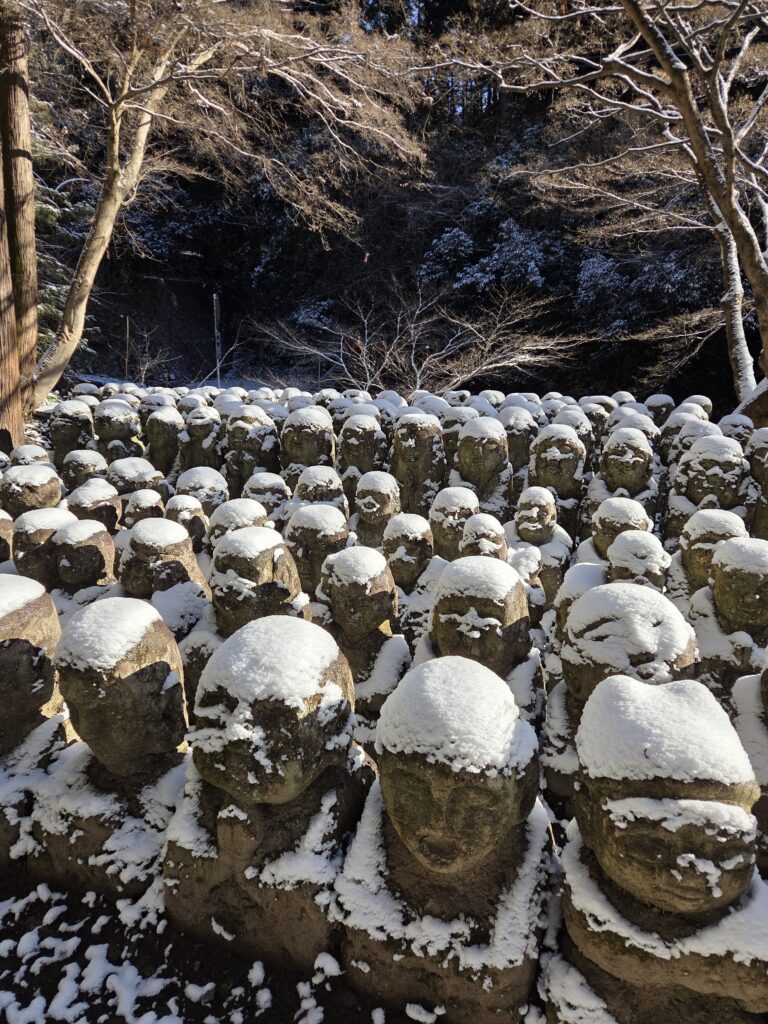 Snow-covered Rakan stone statues at Otagi Nenbutsuji Temple in Kyoto, creating a peaceful winter scene.