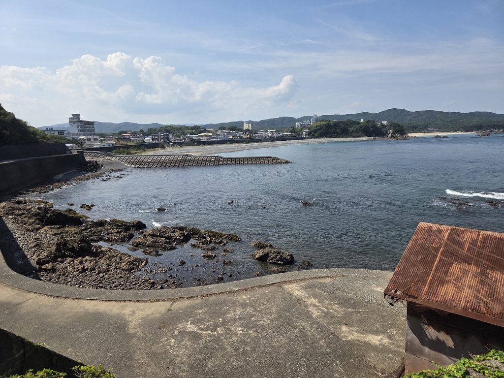 Looking out from the rocky shoreline near Kujirazaki cape, the fishing town of Osatsu curves along the bay beyond a tetrapod breakwater. This quiet stretch of coast, home to Osatsu's Ama divers, is part of a scenic walking trail along the cape.